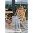 Couverture tissée gris clair à motif géométrique blanc sur chaise pliante en teck