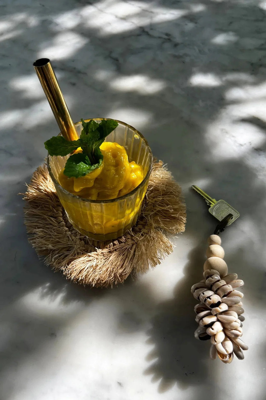 Verre de jus d’ananas jaune avec menthe et paille dorée sur sous-verre rond en raphia naturel à franges solaires