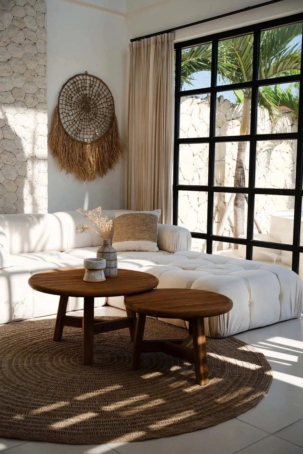 Salon cosy avec sofa blanc, tables rondes en bois et vue tropicale, mural rond en raphia