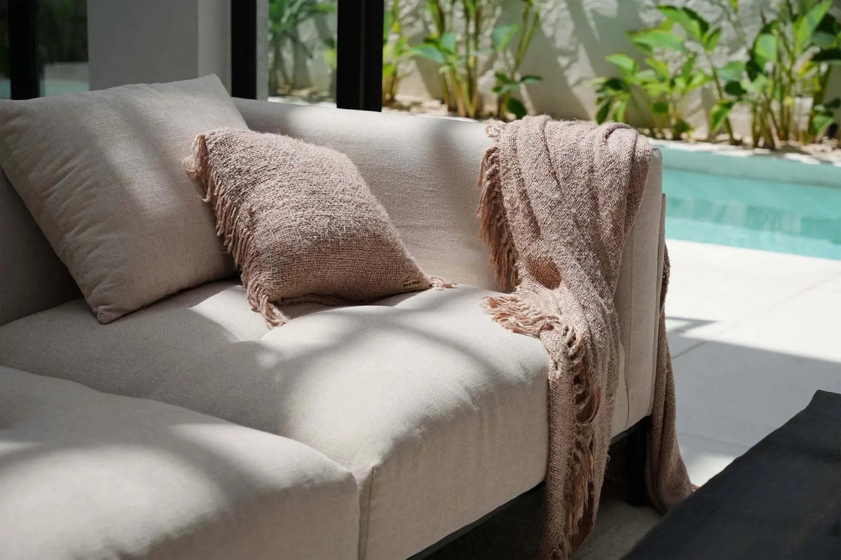 Canapé en lin beige avec coussin texturé et couverture frangée assortie drapée sur l’accoudoir