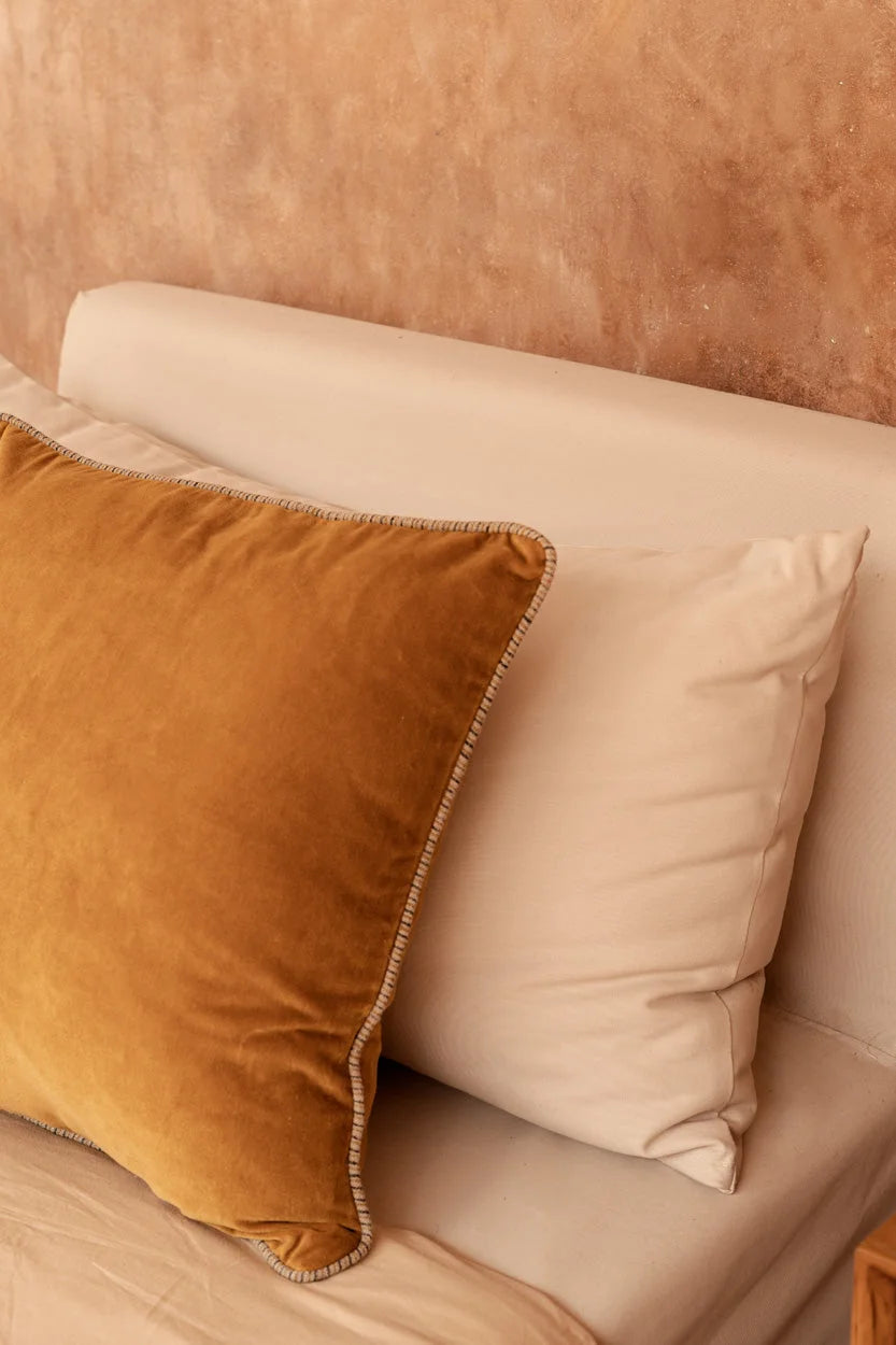 Coussin en velours jaune moutarde avec passepoil texturé sur lit crème