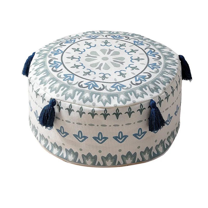 Housse de pouf rond avec un motif bleu et blanc, ornée de pompons, idéale pour une touche bohème chic.