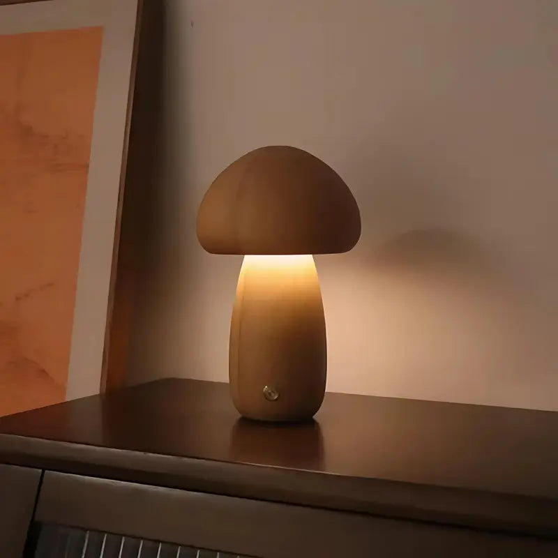 Petite lampe champignon en bois, allumée et posée sur un meuble en bois foncé.