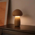 Petite lampe champignon en bois, allumée et posée sur un meuble en bois foncé.