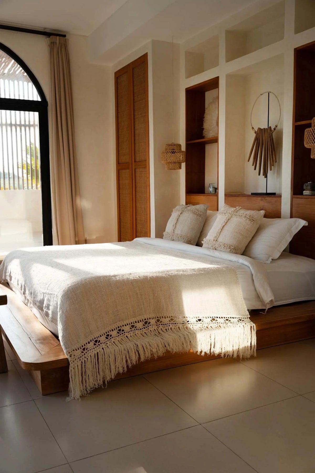 Lit en bois avec linge blanc et coussins décoratifs, plaid en coton beige à franges