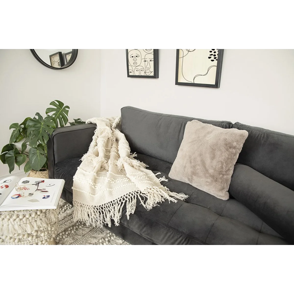 Canapé en velours gris foncé avec plaid en laine écrue à franges et motifs en relief