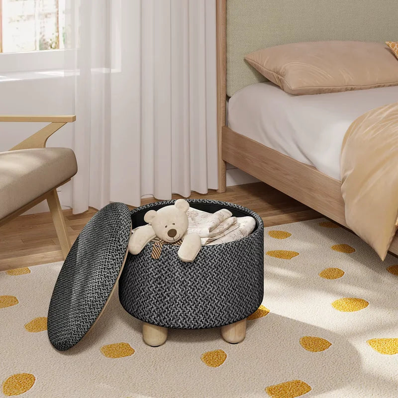 Pouf de rangement rond noir dans une chambre d’enfant, utilisé pour ranger jouets et accessoires.